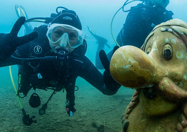 Zwei Taucher beim Tauchen mit Sauerstoff entdecken am Seeboden eine Obelix-Figur.