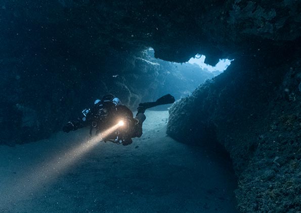 Ein Taucher mit einem Scheinwerfer erkundet eine Höhle am Meeresgrund.